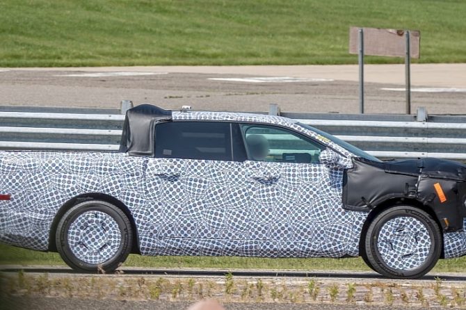 Ford Fathom electric pickup in black and white camouflage wrap beside a highway guardrail
