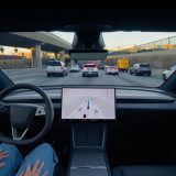 Driver's view of a Tesla Model Y L on FSD in highway traffic, hands resting in lap
