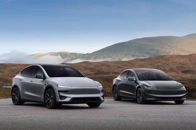 Silver Tesla Model Y and dark grey Model 3 parked on pavement in front of brown hills and a misty mountain