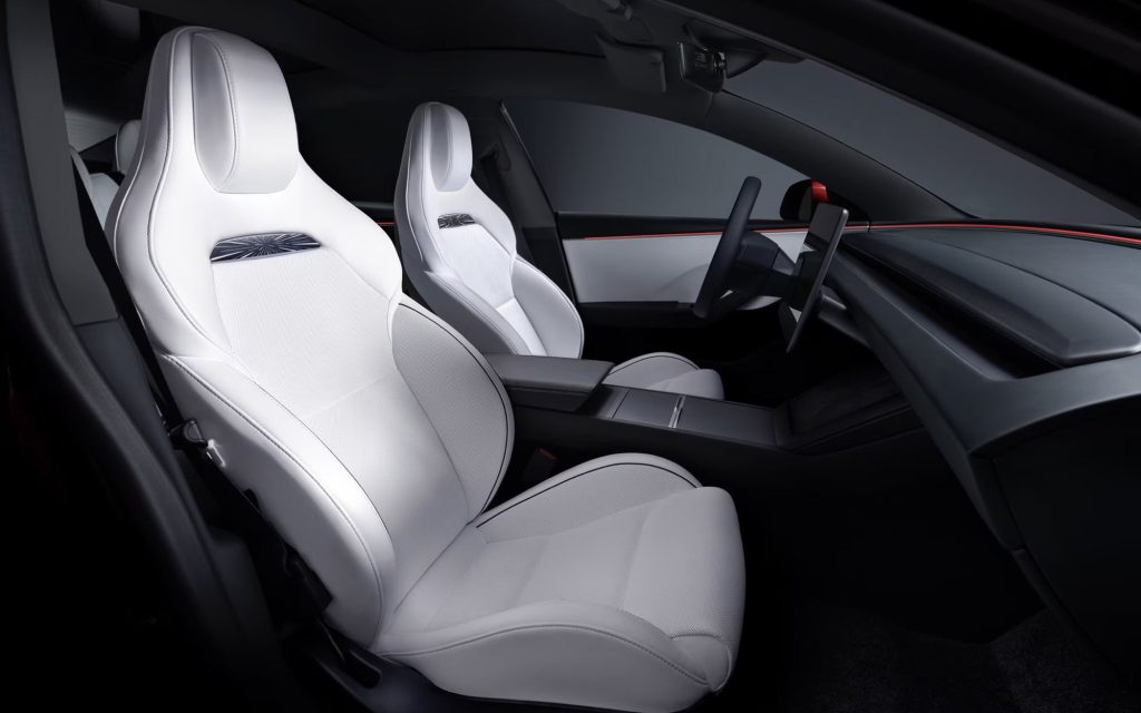 Tesla cabin with white sport front seats, black dashboard, central touchscreen and red ambient light strip
