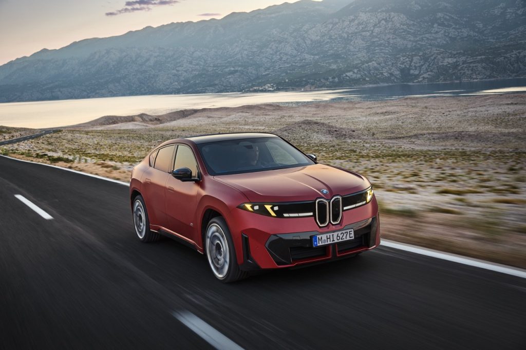 Red BMW iX4 M60 driving on a coastal road