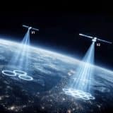 Illustration of two Starlink satellites labelled V1 and V2 beaming signal coverage onto Earth at night