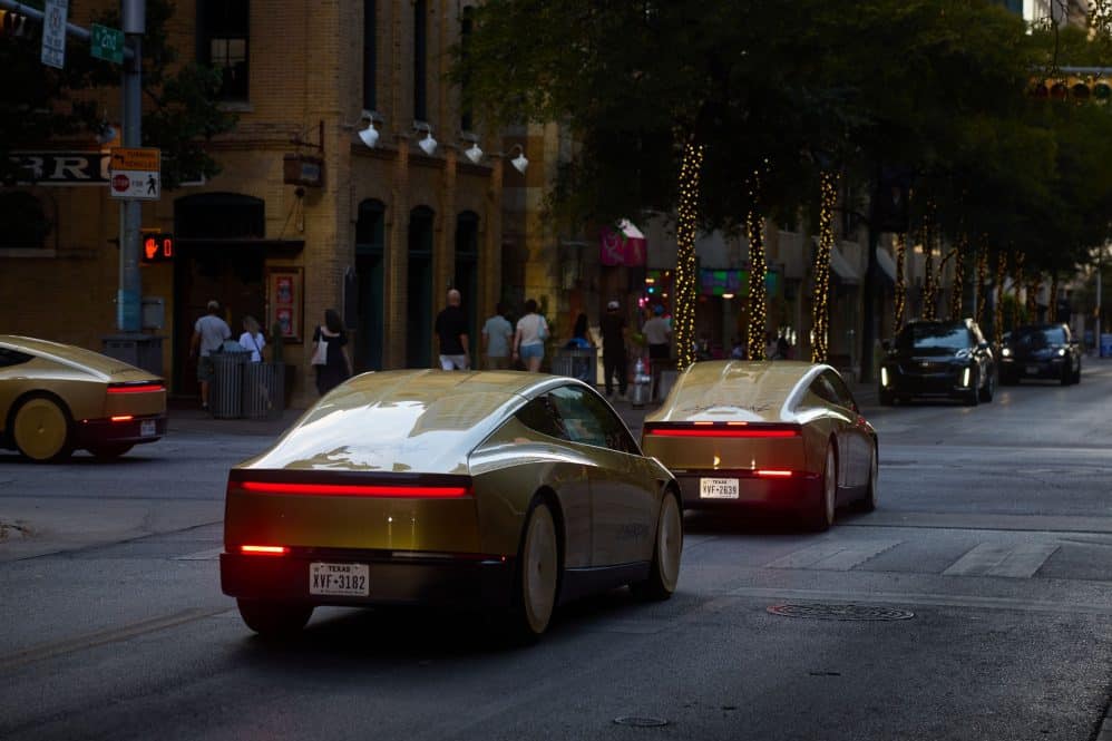 Gold Tesla Cybercabs driving on a downtown Austin street at dusk