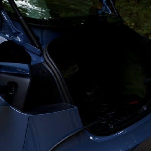 A Tesla Mobile Connector cable plugged into a blue Tesla's charge port beside an open trunk