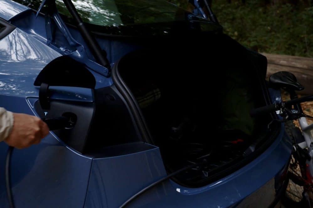 A Tesla Mobile Connector cable plugged into a blue Tesla's charge port beside an open trunk