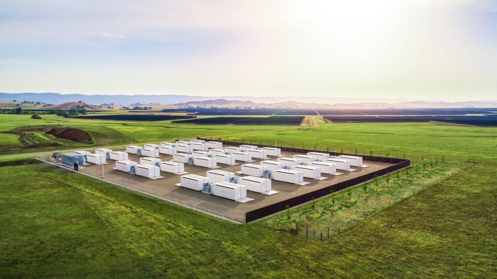 Rows of Tesla Megapack battery units at an energy storage site in a green field