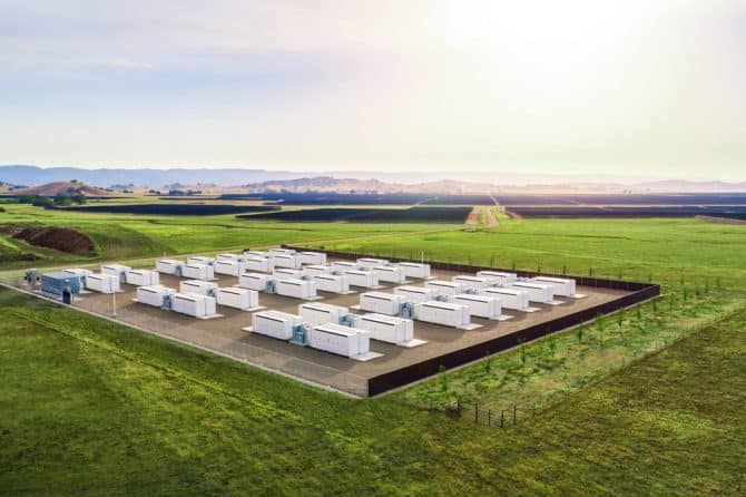 Rows of Tesla Megapack battery units at an energy storage site in a green field