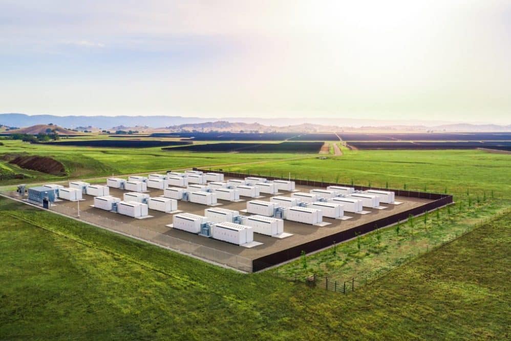 Rows of Tesla Megapack battery units at an energy storage site in a green field