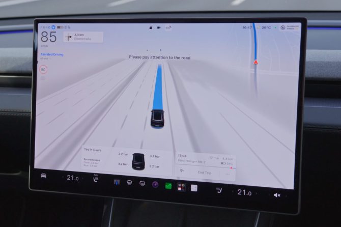 Tesla touchscreen showing Assisted Driving engaged at 85 km/h on a highway, with a 'Please pay attention to the road' message