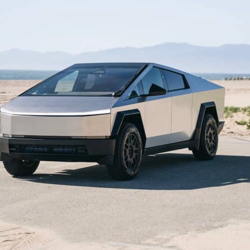 Silver Tesla Cybertruck parked beside a beach with mountains in the background