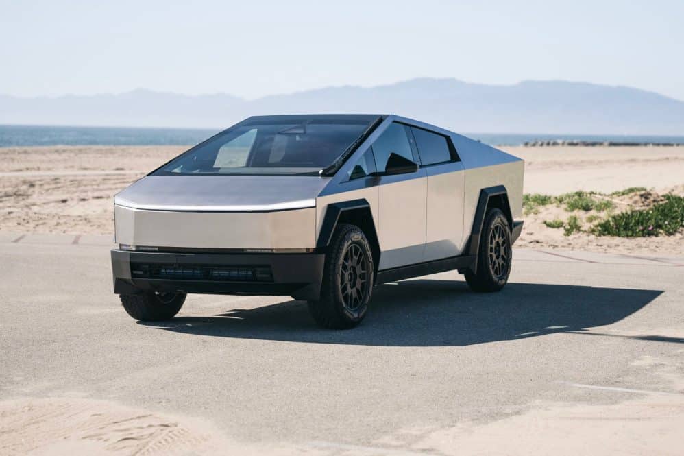 Silver Tesla Cybertruck parked beside a beach with mountains in the background