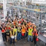 Tesla employees in hard hats and safety vests cheer in front of the first-generation Optimus humanoid robot production line in Fremont, California