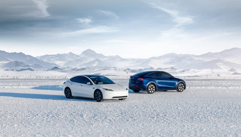 White Tesla Model 3 and blue Model Y parked on snow in front of mountains