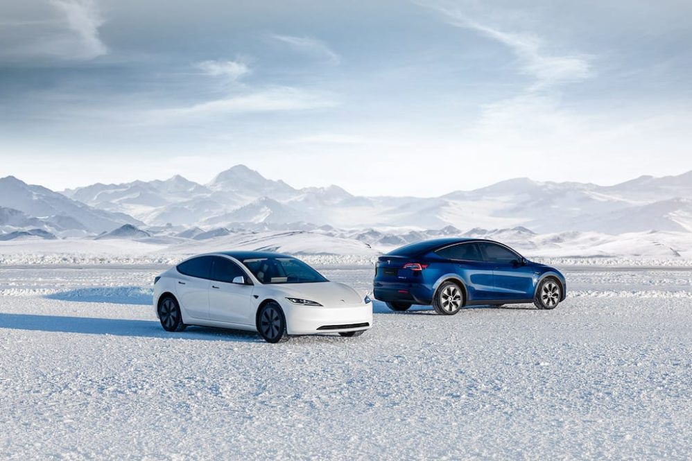 White Tesla Model 3 and blue Model Y parked on snow in front of mountains